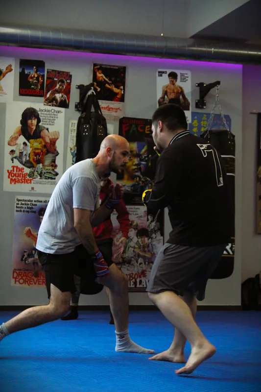 Two practitioners squaring up in fighting stance during a class at Be Water Lisboa, with martial-arts movie posters in the background