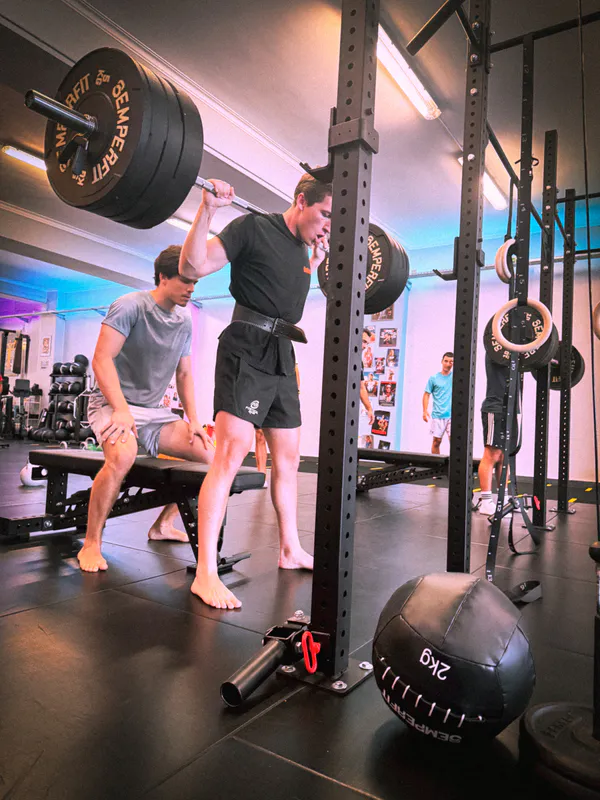 Athlete lifting a barbell with a coach spotting at Be Water Lisboa
